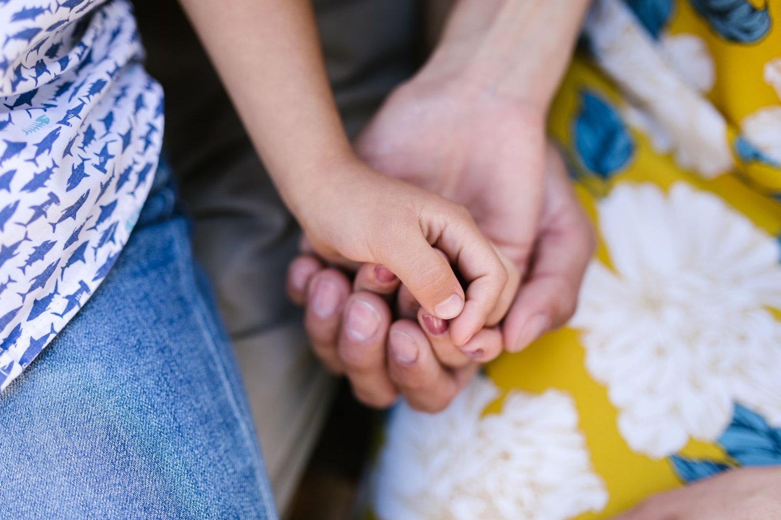 Close das mãos de uma criança e de um adulto unidas, sem rostos à mostra