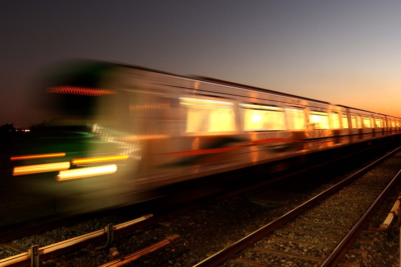 Trem do Metrô-DF em movimento ao entardecer, em foto de longa exposição ao lado dos trilhos