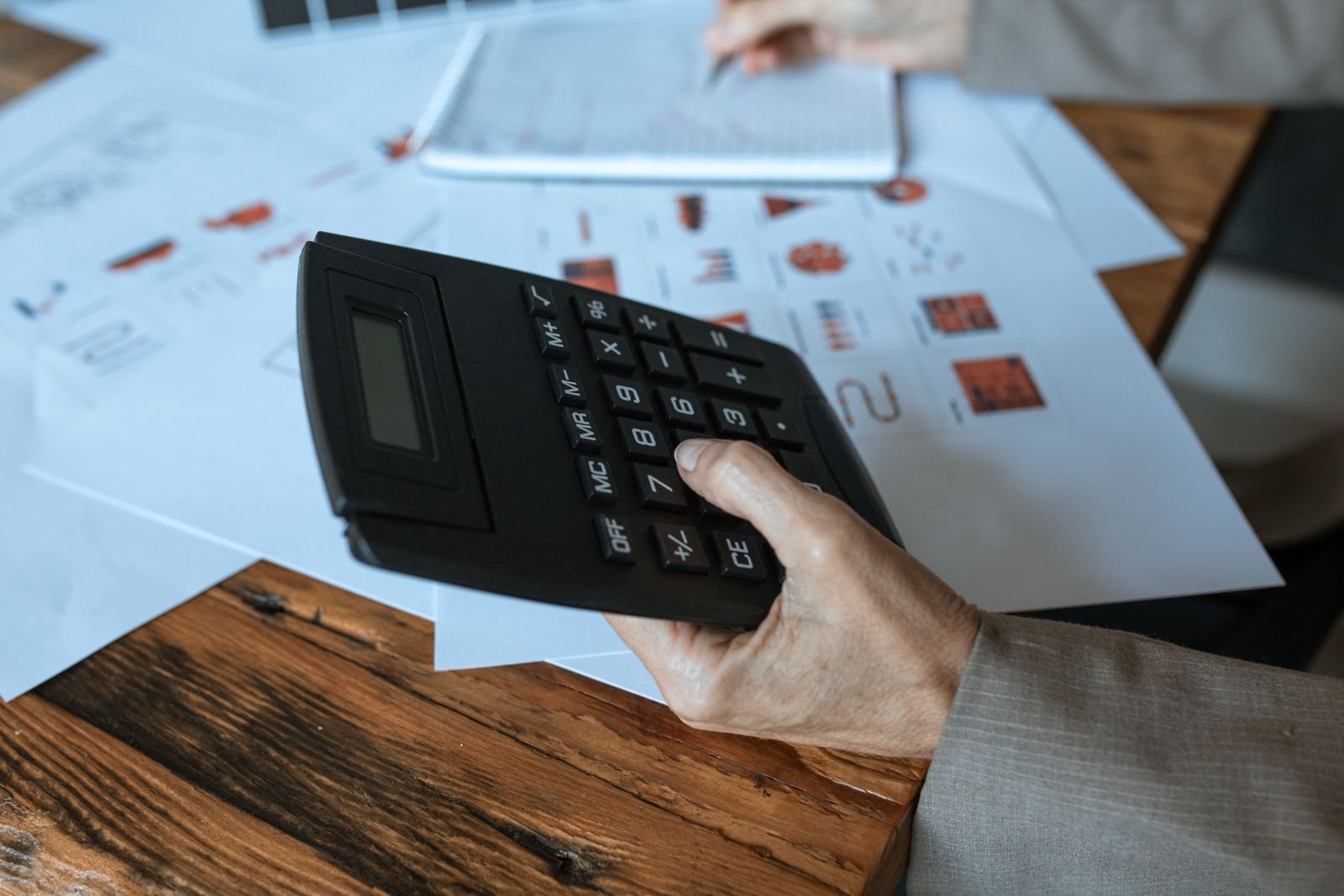 Mão segura calculadora sobre mesa com papéis e gráficos, imagem ilustrativa