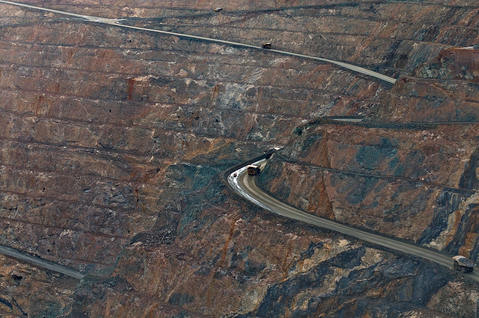 Vista aérea de mina a céu aberto com caminhões fora de estrada em estrada em espiral; foto ilustrativa