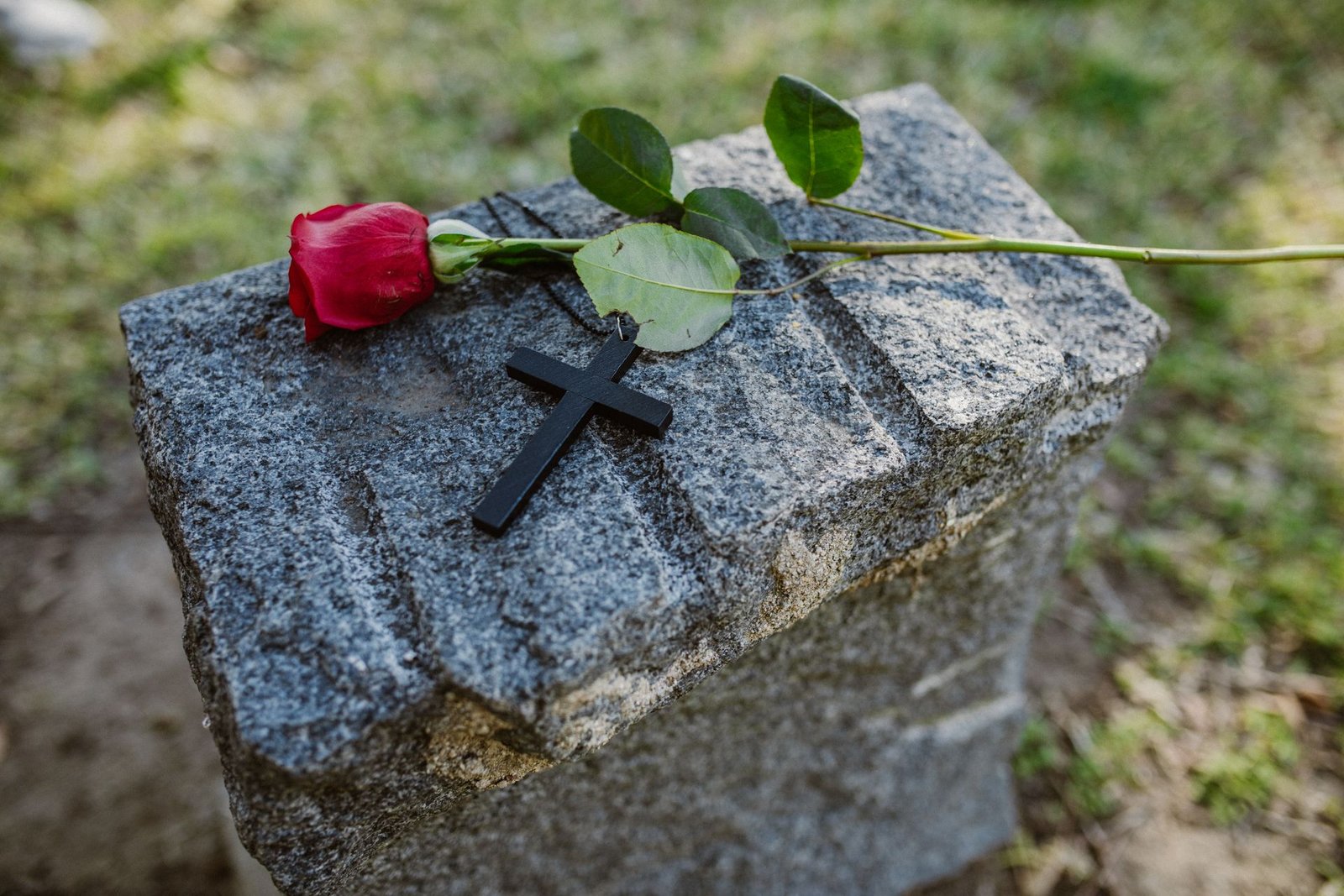 Rosa vermelha e crucifixo preto sobre lápide de granito em cemitério