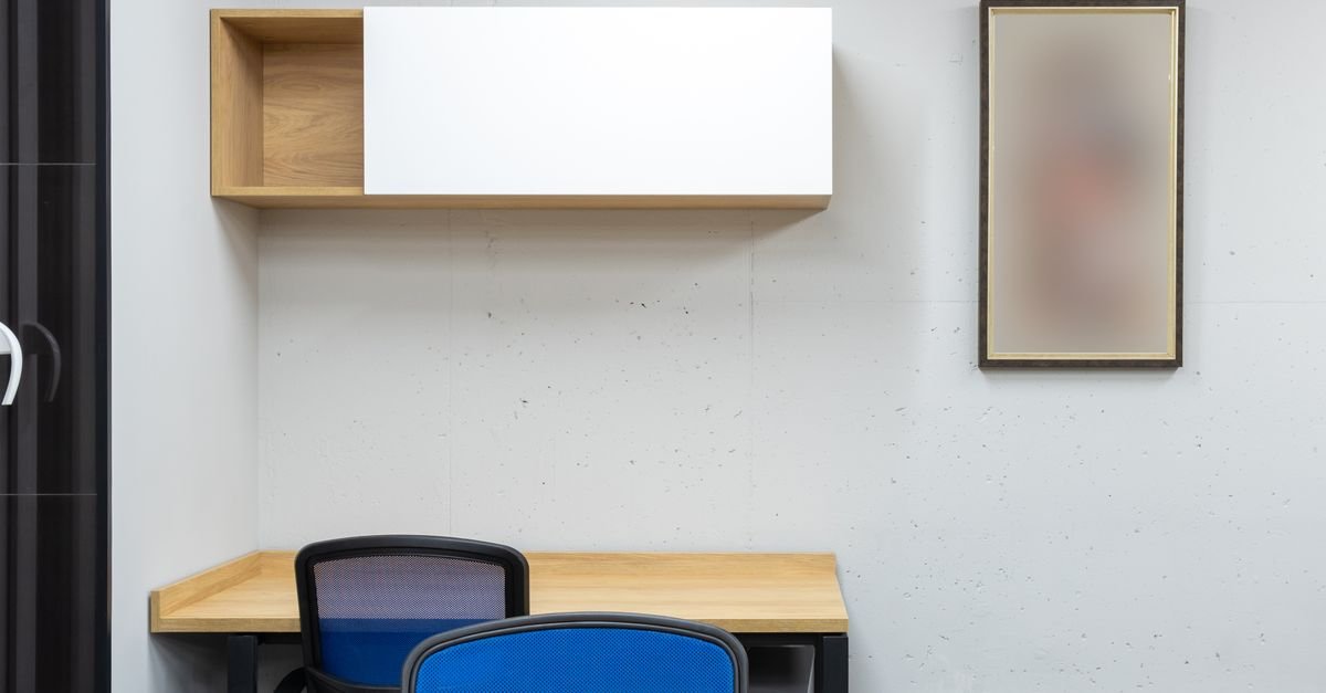 Mesa de madeira com duas cadeiras de escritório azuis e armário suspenso em sala vazia