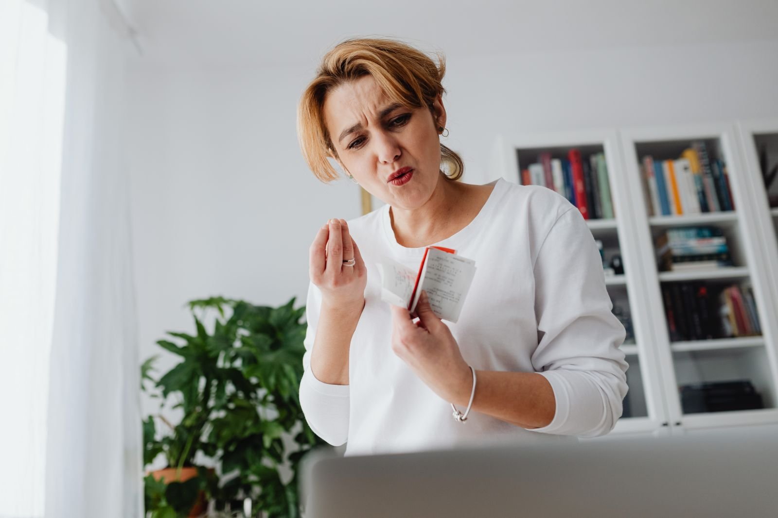 Mulher confere recibos diante de um notebook com expressão preocupada; foto ilustrativa