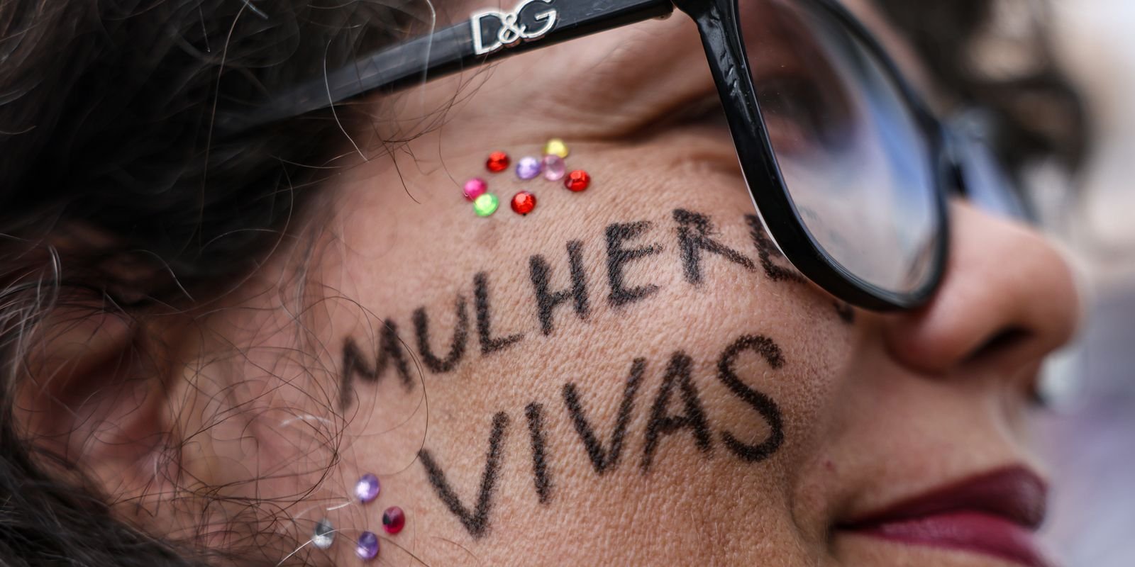 Mulher com a frase 'Mulheres vivas' escrita no rosto durante ato contra o feminicídio em Brasília