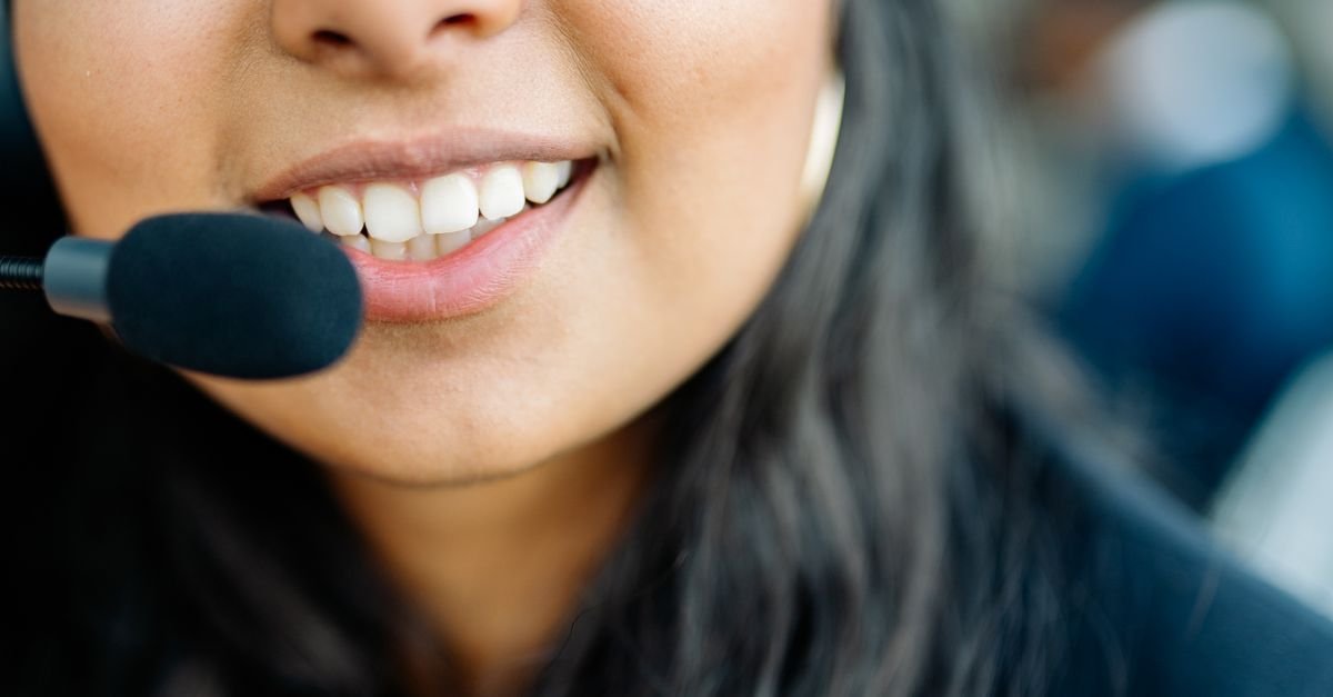 Close do rosto de uma atendente sorrindo, com fone de ouvido e microfone, em atendimento telefônico; foto ilustrativa