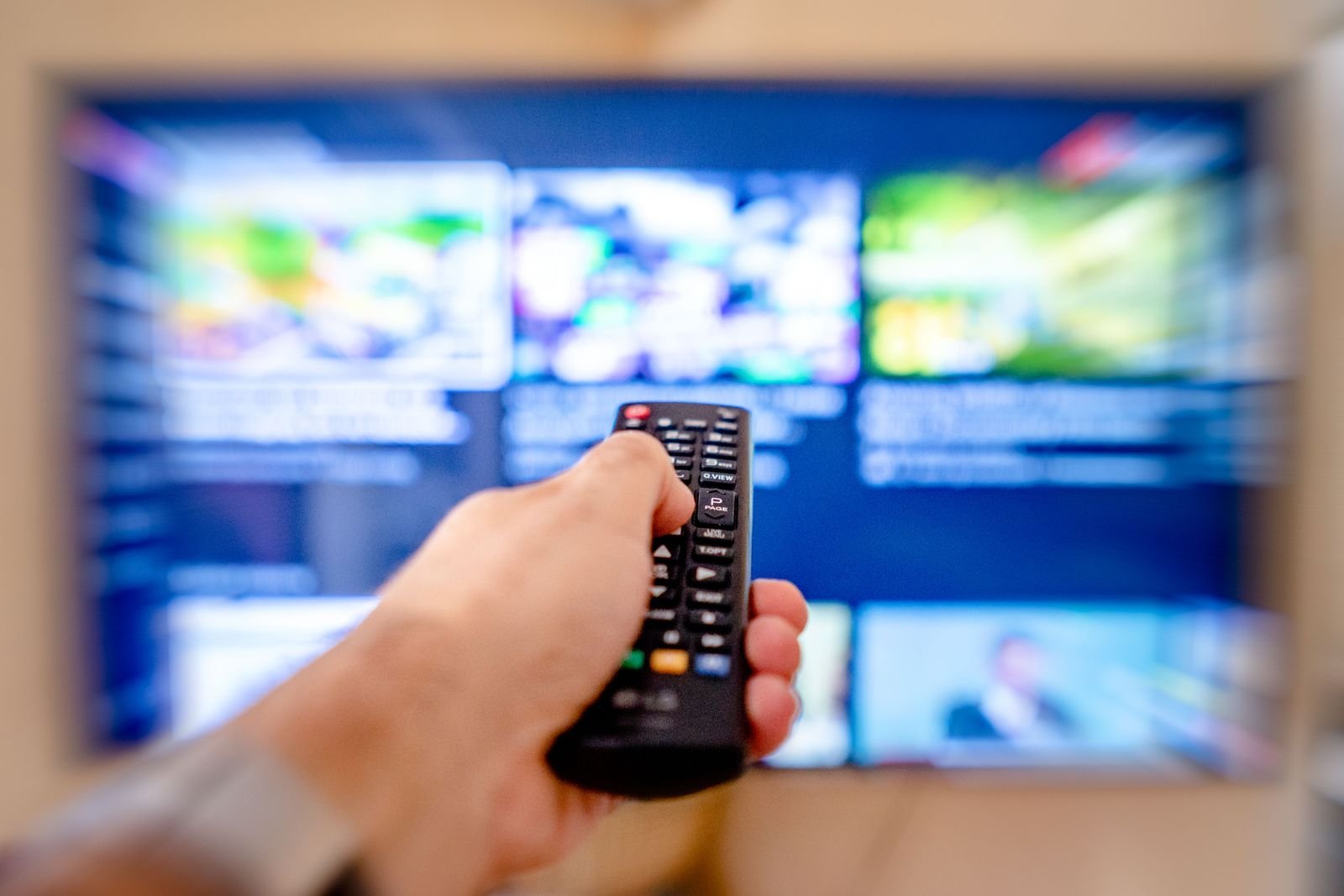 Mão segura controle remoto apontado para uma televisão com catálogo de streaming desfocado