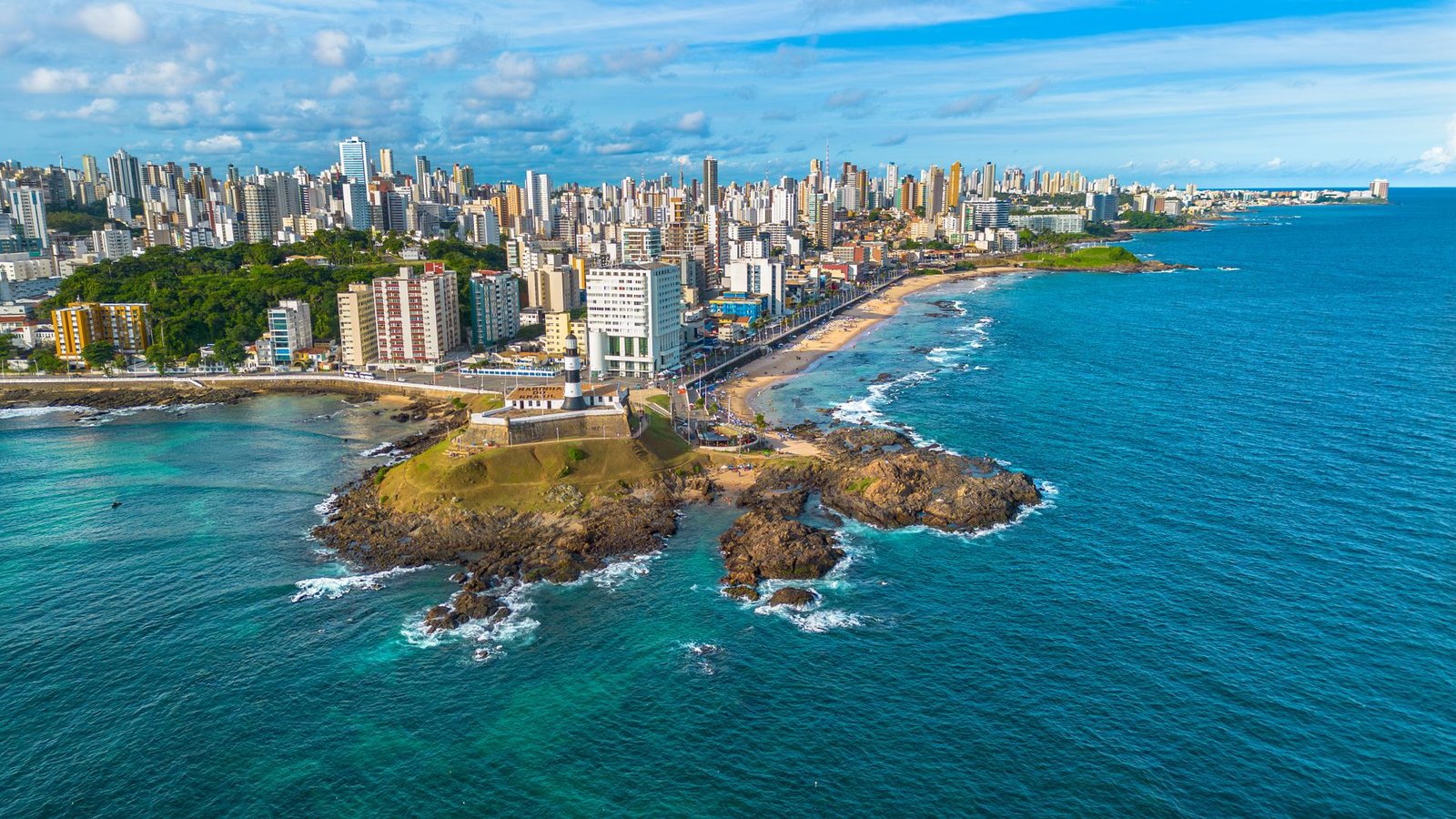 Vista aérea da orla de Salvador, com o Farol da Barra e prédios ao fundo