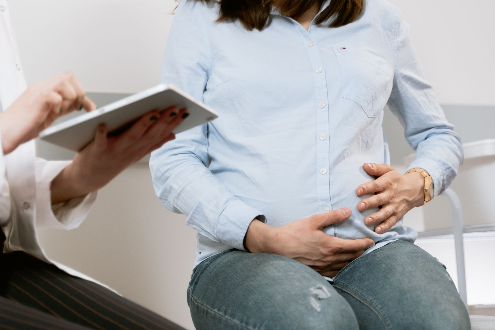 Gestante com as mãos sobre a barriga durante consulta em que a profissional usa um tablet