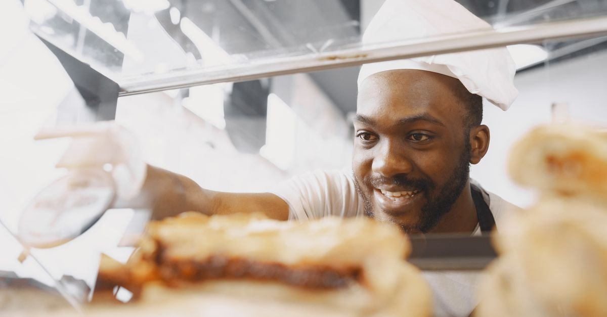 Padeiro sorridente arruma pães na vitrine de uma padaria, em imagem ilustrativa de pequeno negócio