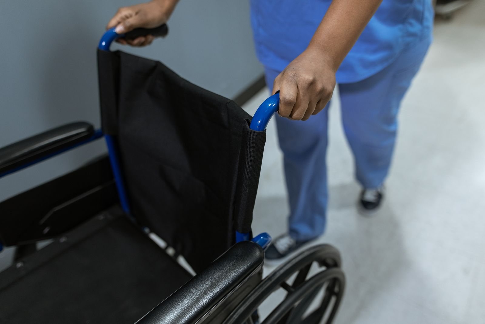 Profissional de saúde empurra cadeira de rodas vazia em corredor de hospital (foto de arquivo)