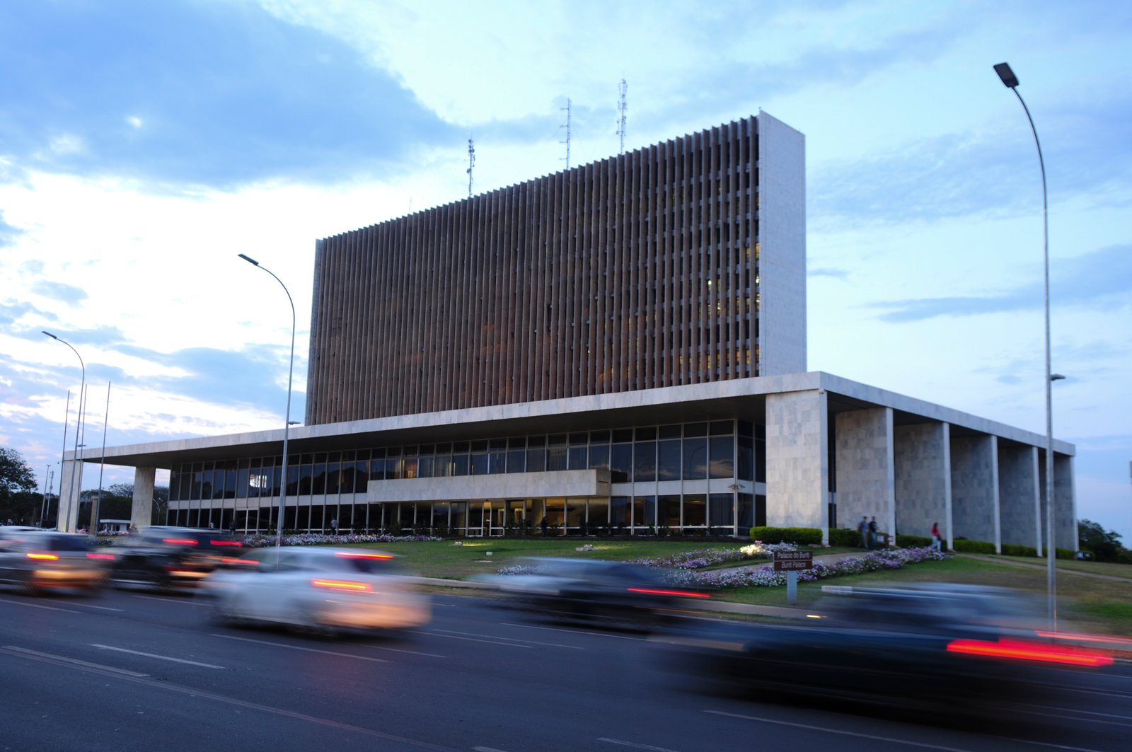 Fachada do Palácio do Buriti, sede do governo do Distrito Federal, ao entardecer, com carros em movimento na via em frente