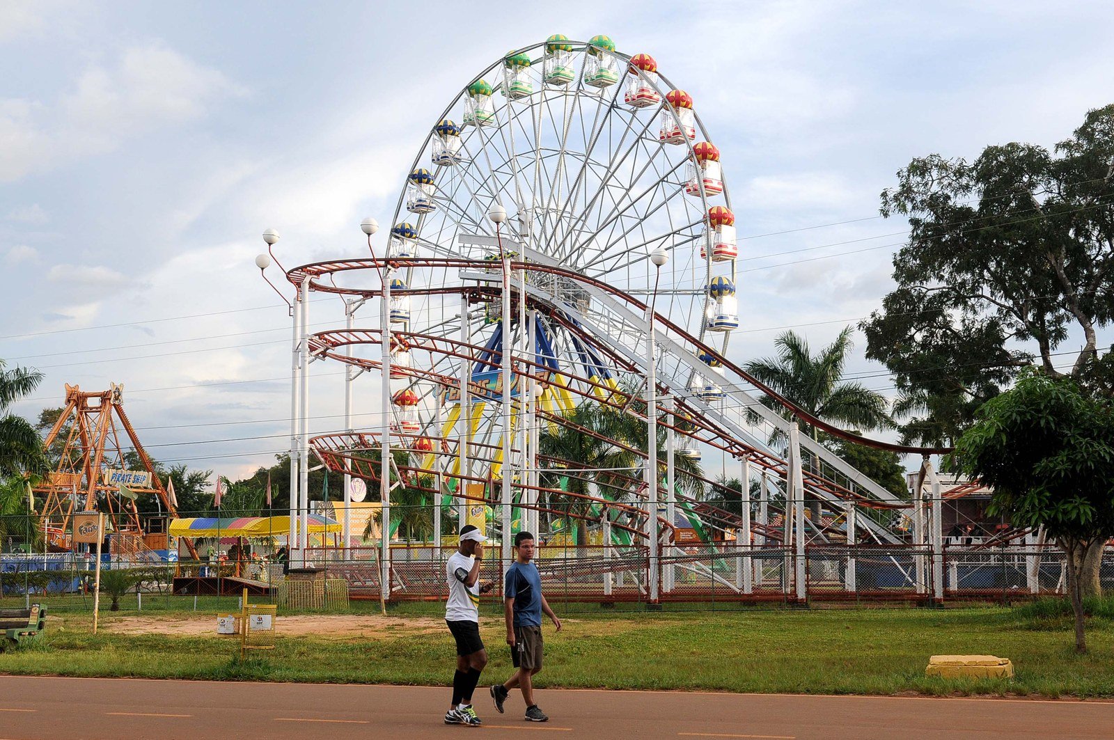 Roda-gigante e brinquedos do parque de diversões do Parque da Cidade, com dois frequentadores caminhando na pista; foto de arquivo
