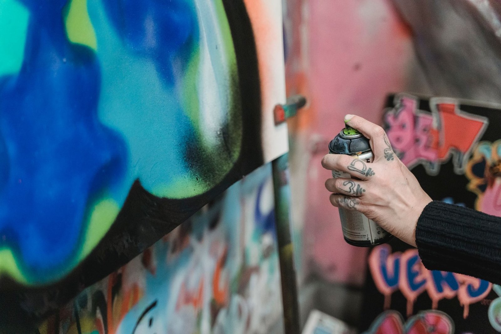 Mão segura lata de spray diante de um muro coberto de grafite (foto ilustrativa)