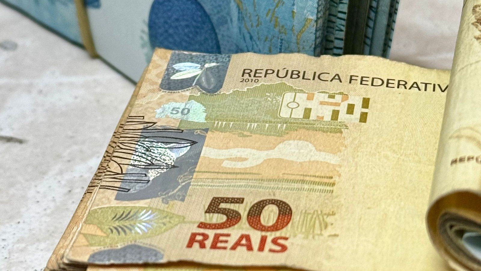 Maços de cédulas de 50 e 100 reais sobre uma superfície clara, foto ilustrativa