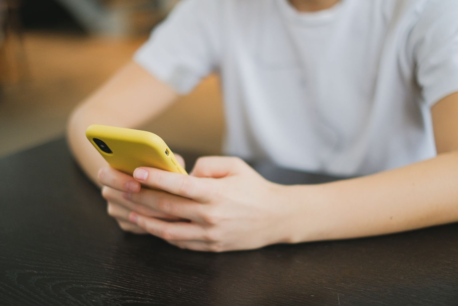 Mãos de uma pessoa seguram um celular com capa amarela sobre uma mesa, foto de arquivo