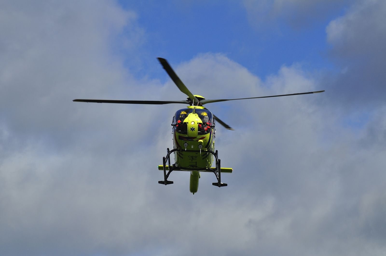 Helicóptero amarelo de resgate aéreo visto de baixo contra um céu com nuvens (imagem ilustrativa)