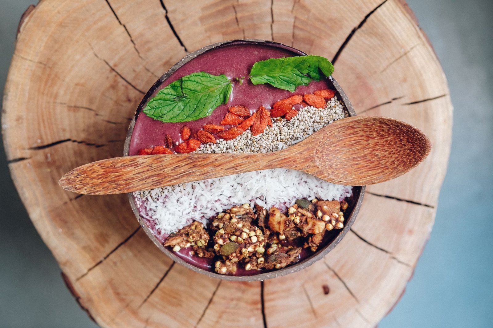 Tigela de açaí em casca de coco com granola, coco ralado e folhas de hortelã sobre tronco de madeira