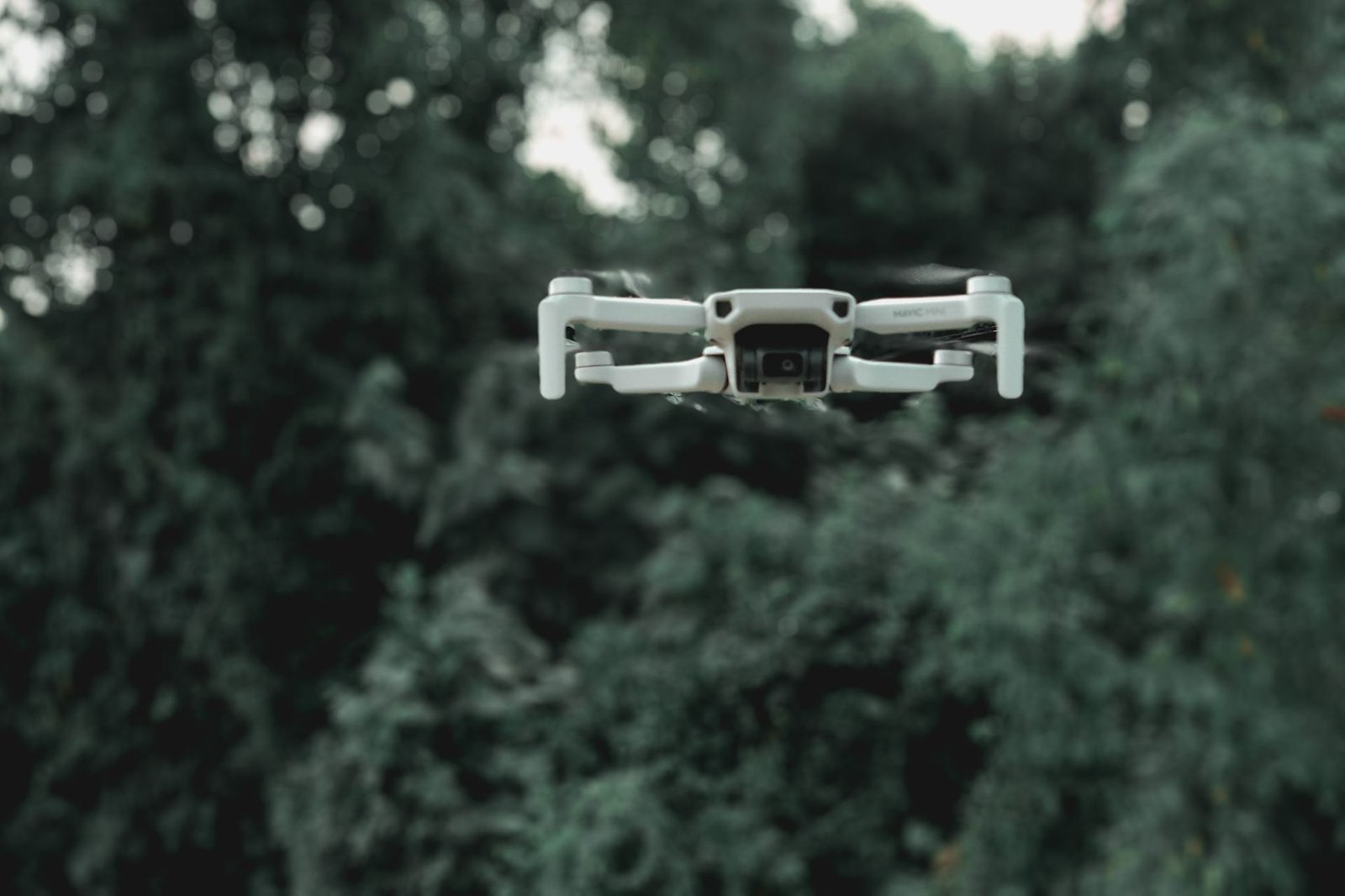 Drone branco em voo diante de vegetação, imagem ilustrativa