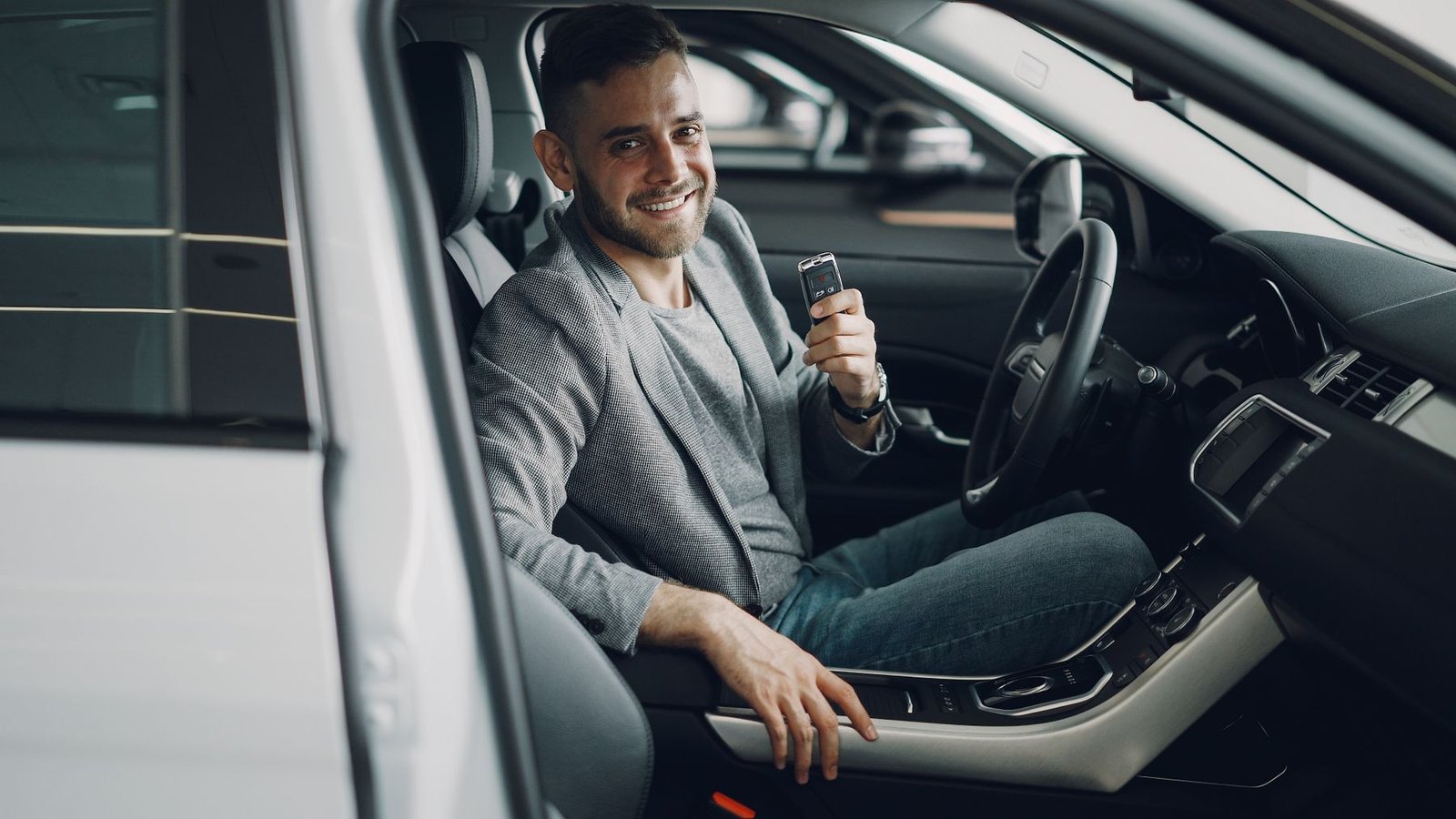 Homem sorridente sentado ao volante de carro novo segurando a chave, em concessionária