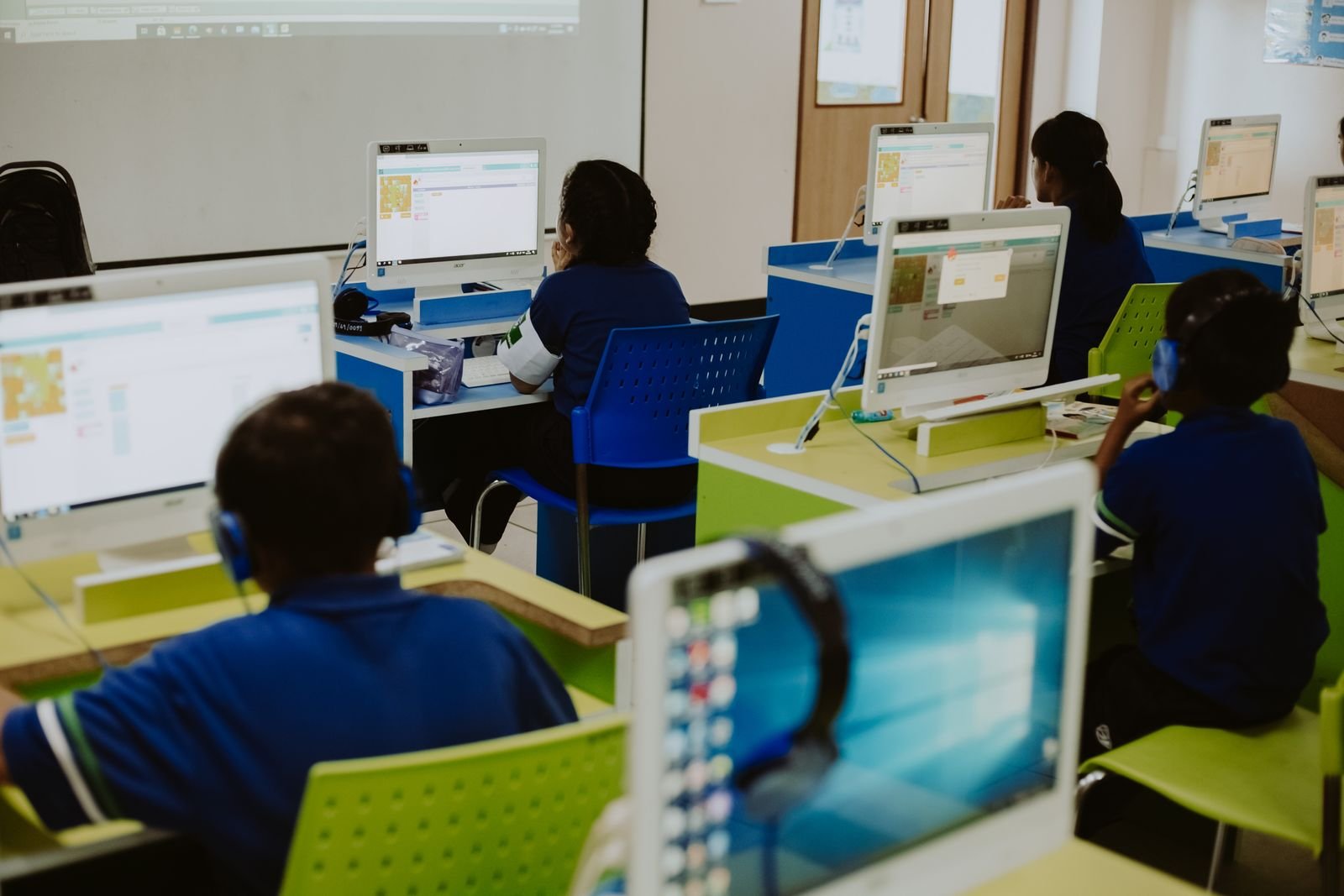 Estudantes diante de computadores em sala de aula de informática, imagem ilustrativa