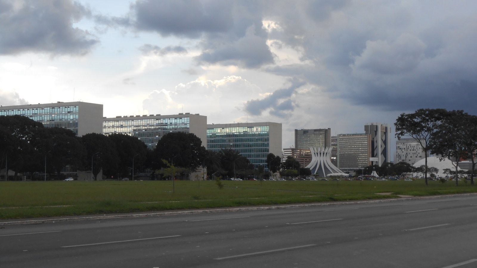 Prédios dos ministérios na Esplanada, em Brasília, com a Catedral ao fundo e céu nublado