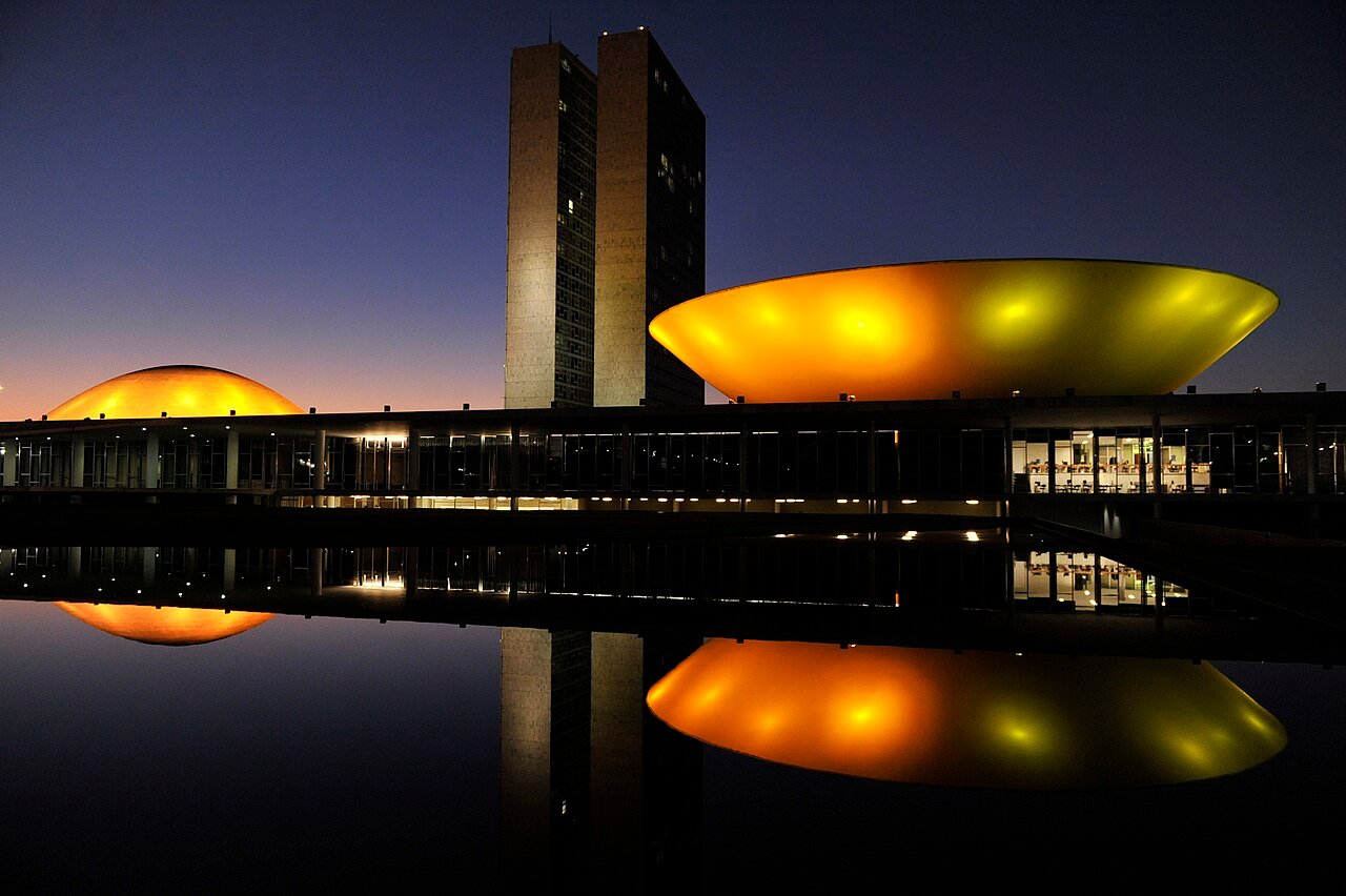 Congresso Nacional em Brasília ao entardecer, com as cúpulas iluminadas em amarelo e as torres ao fundo