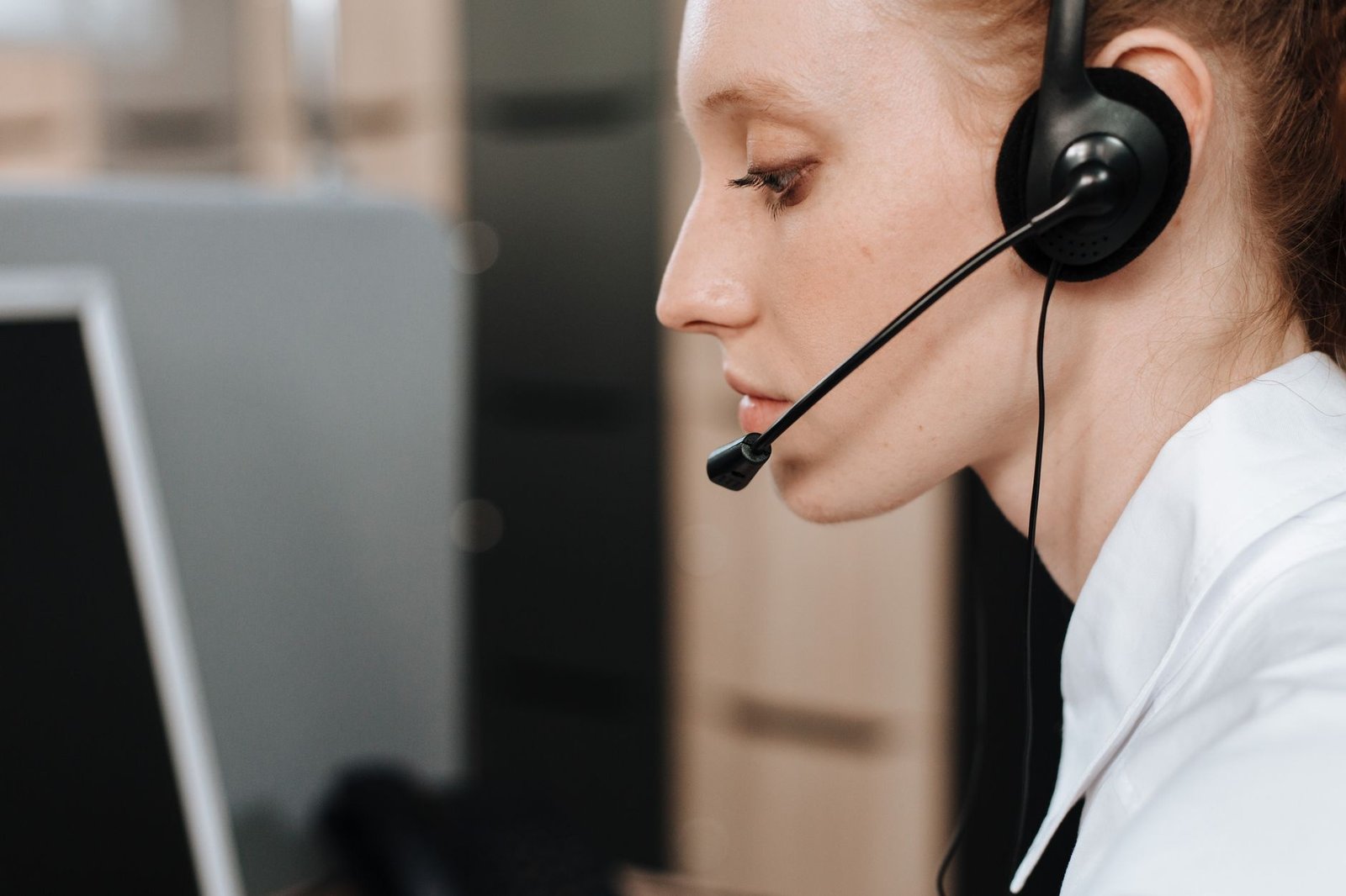 Atendente de call center de perfil, com fone de ouvido e microfone, diante de um monitor (foto ilustrativa de banco de imagens)