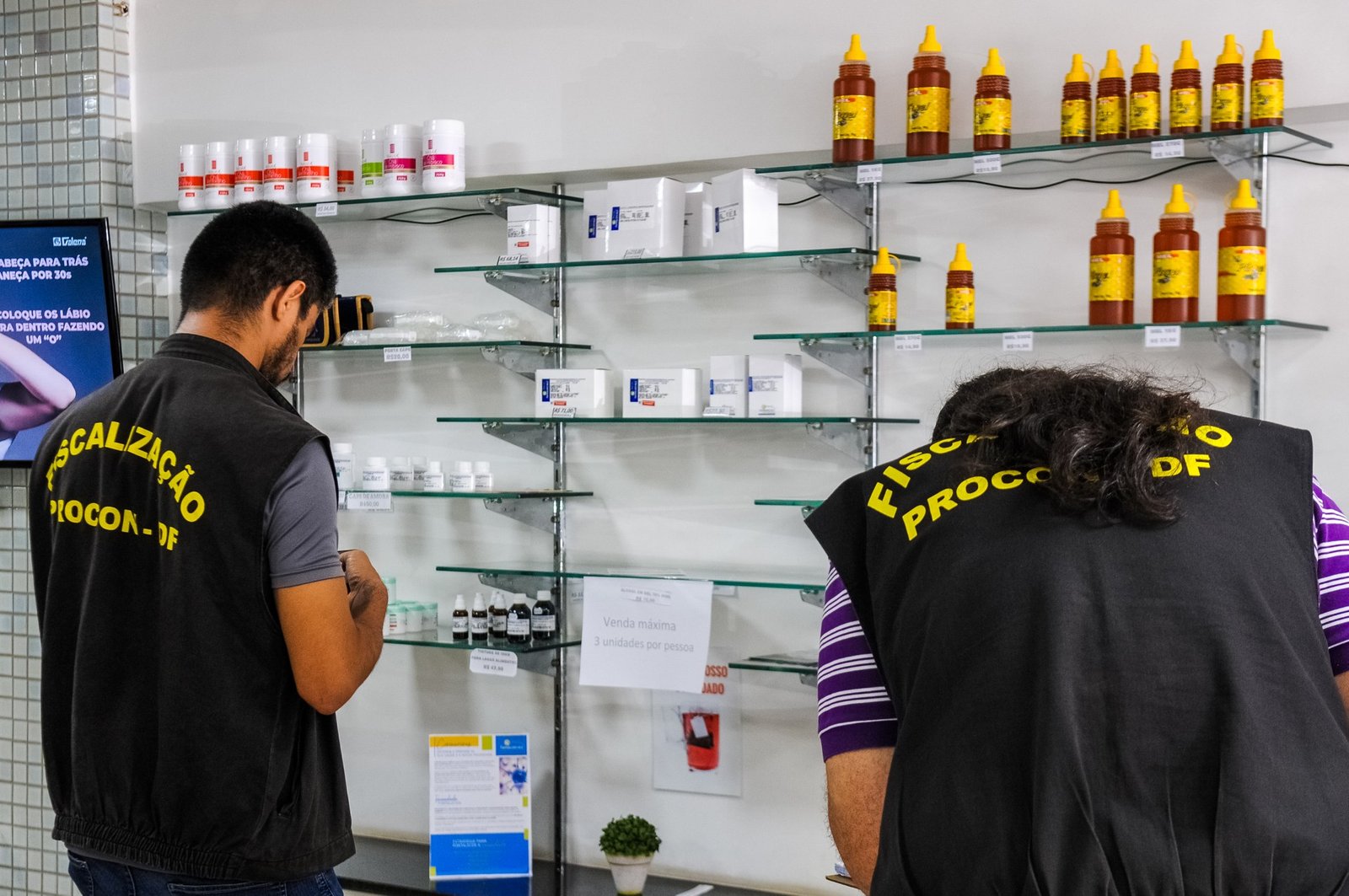 Dois fiscais de colete preto com a inscrição Fiscalização Procon-DF conferem produtos nas prateleiras de uma loja, em 2020