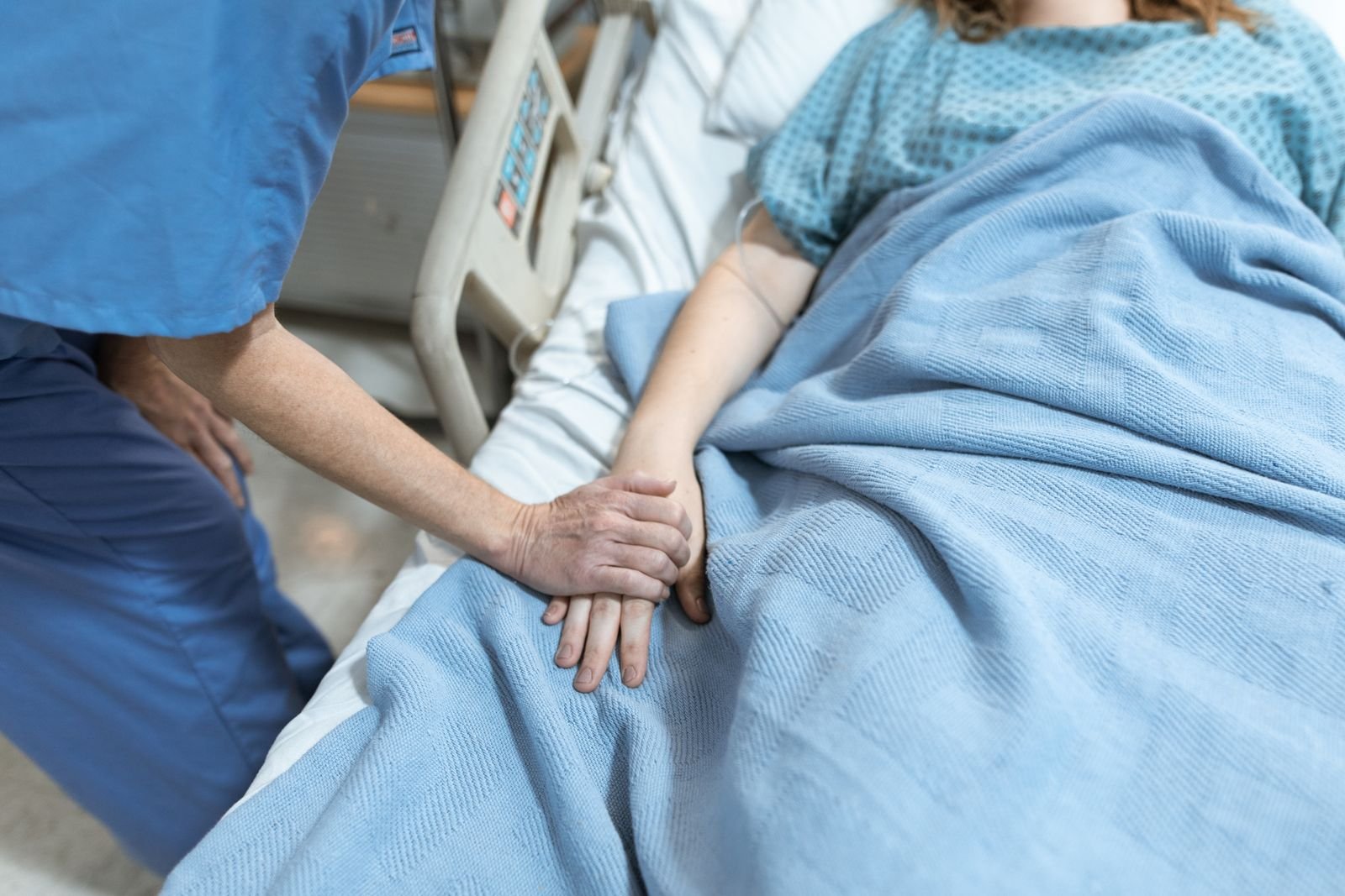 Profissional de saúde de uniforme azul segura a mão de paciente deitada em leito hospitalar (foto ilustrativa)