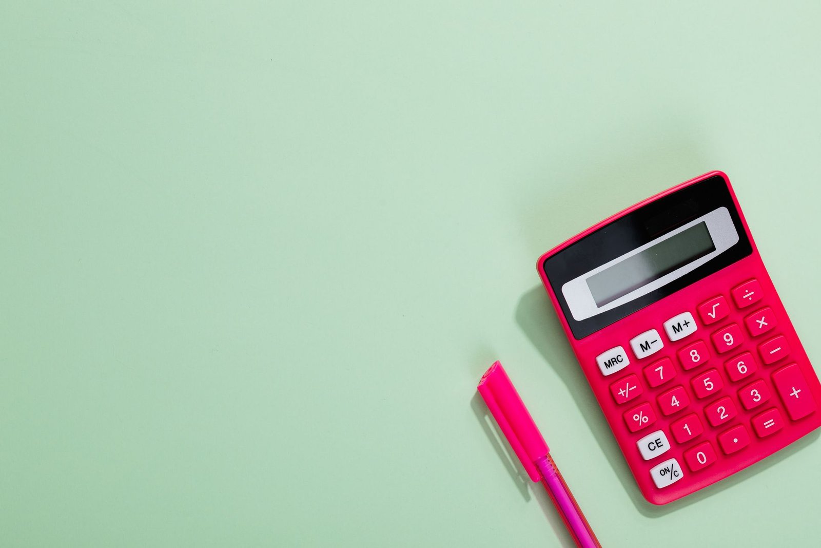 Calculadora rosa e caneta sobre fundo verde, imagem de arquivo