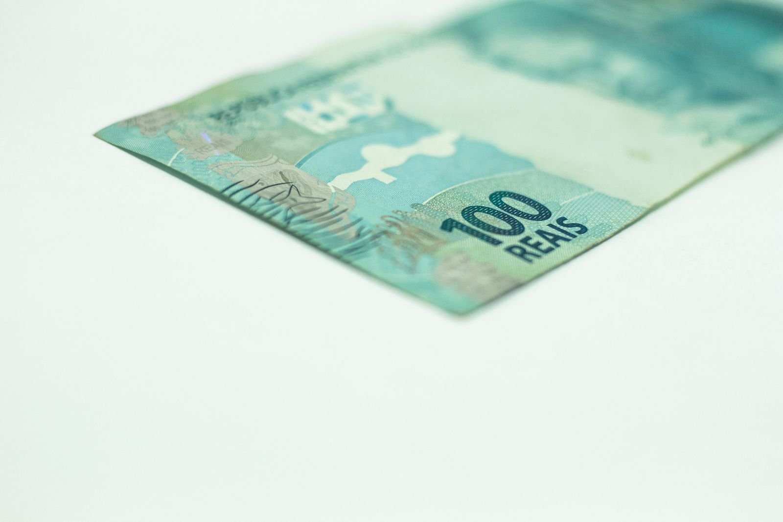 Canto de uma cédula de 100 reais sobre fundo branco, com a legenda 100 REAIS em destaque