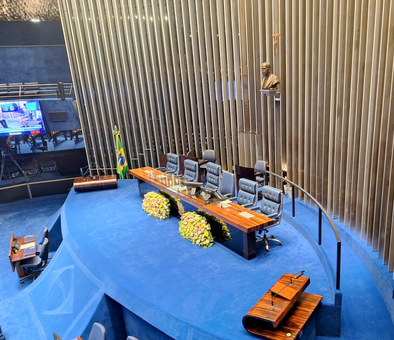 Mesa diretora do plenário do Senado Federal, vista de cima, com flores sobre a bancada