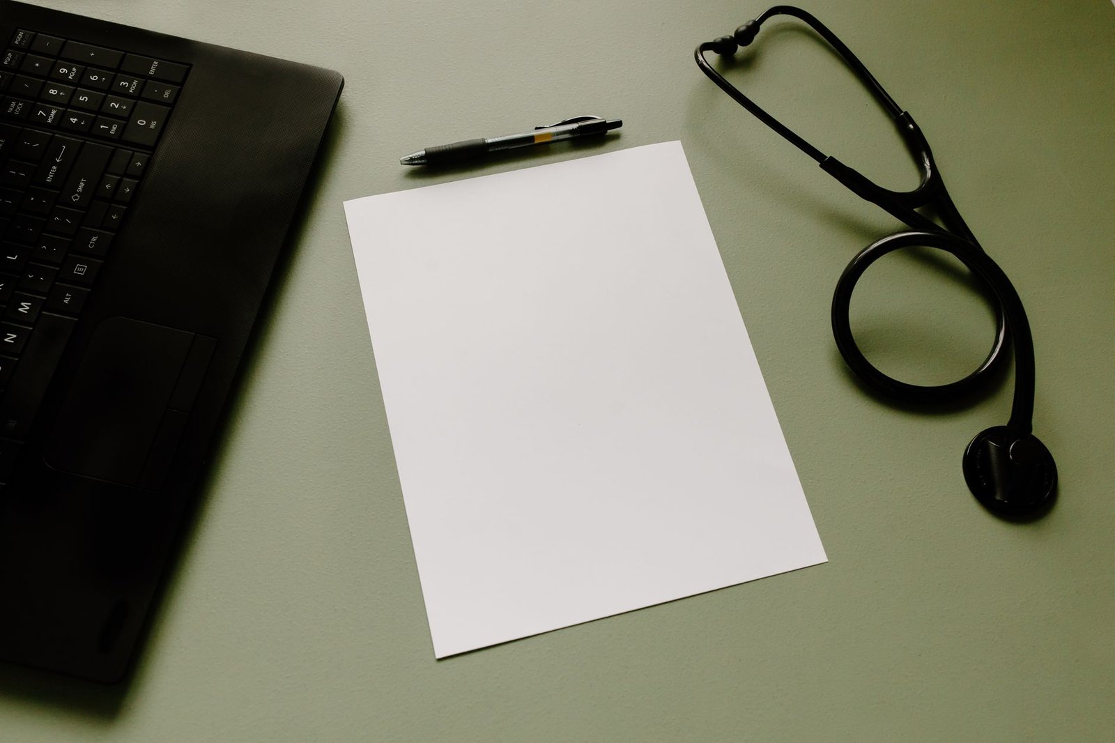 Estetoscópio, folha em branco, caneta e notebook sobre uma mesa