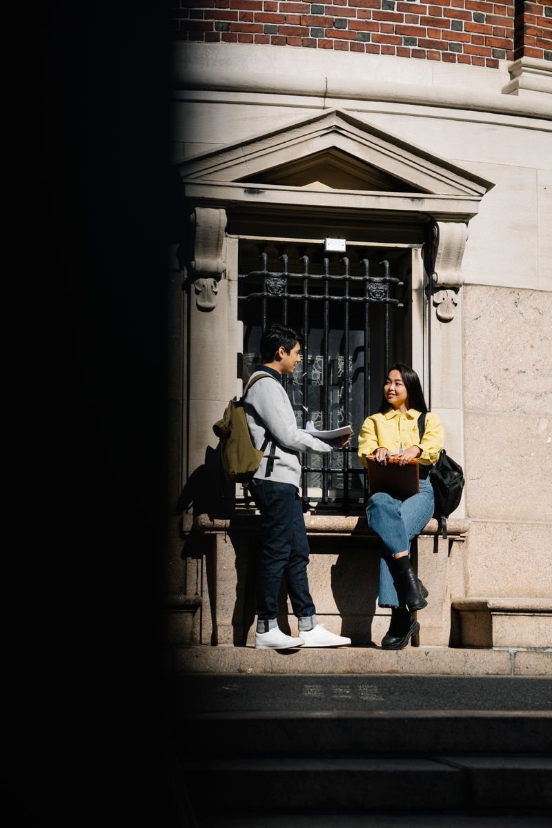 Dois jovens universitários conversando em frente a um prédio histórico de tijolos