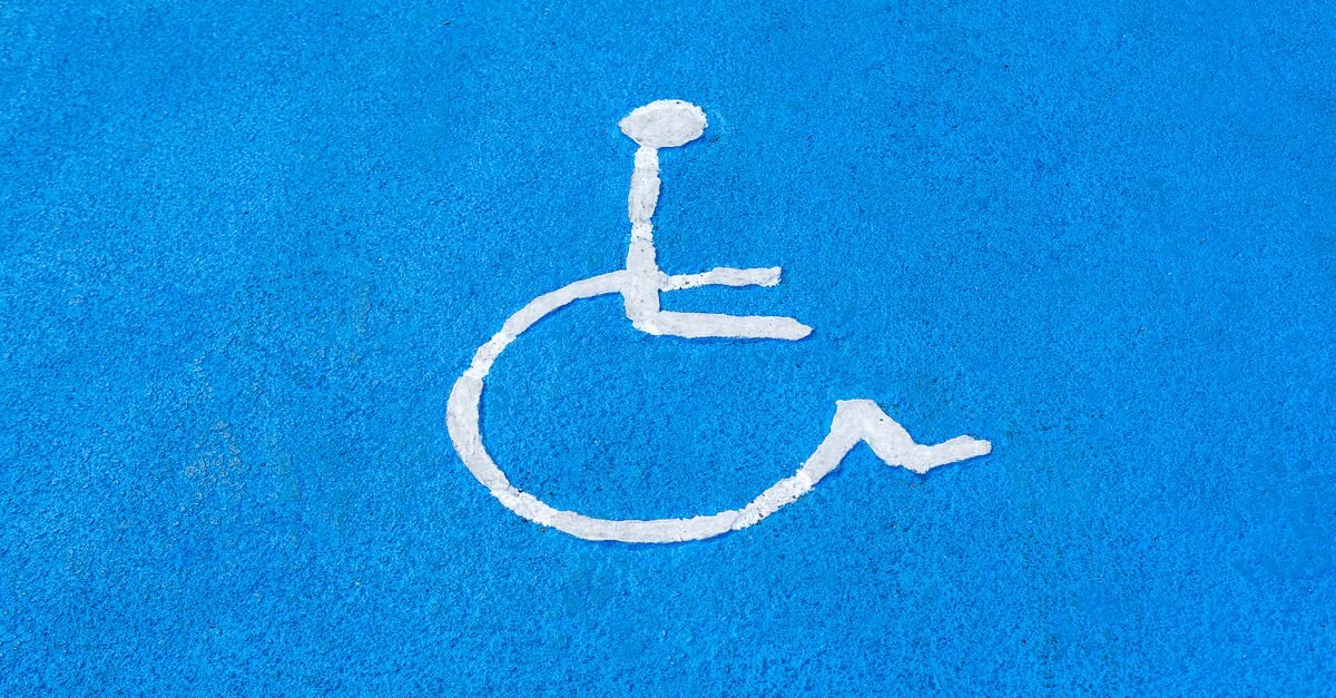 Símbolo de acessibilidade pintado de branco sobre piso azul de vaga de estacionamento
