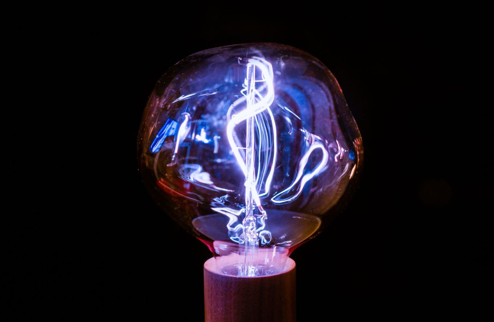 Lâmpada incandescente acesa, com filamento luminoso, sobre fundo escuro (imagem ilustrativa)