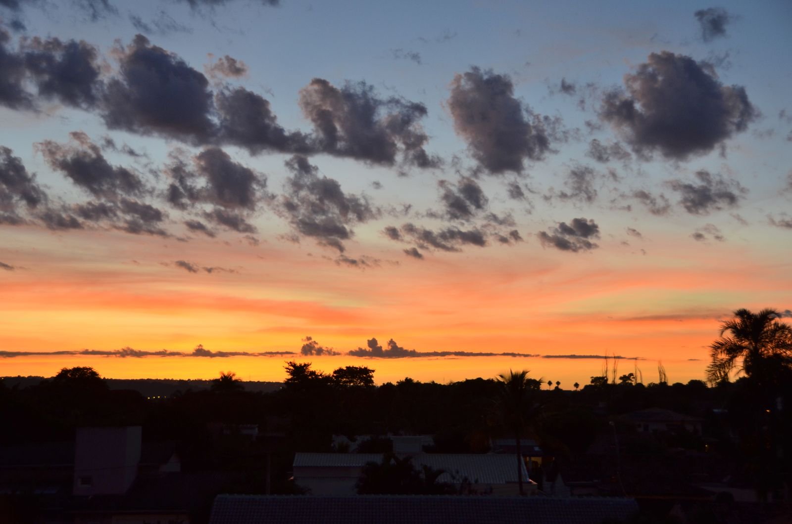 Nuvens escuras contra o céu alaranjado ao entardecer sobre telhados e árvores de Brasília, em foto de arquivo