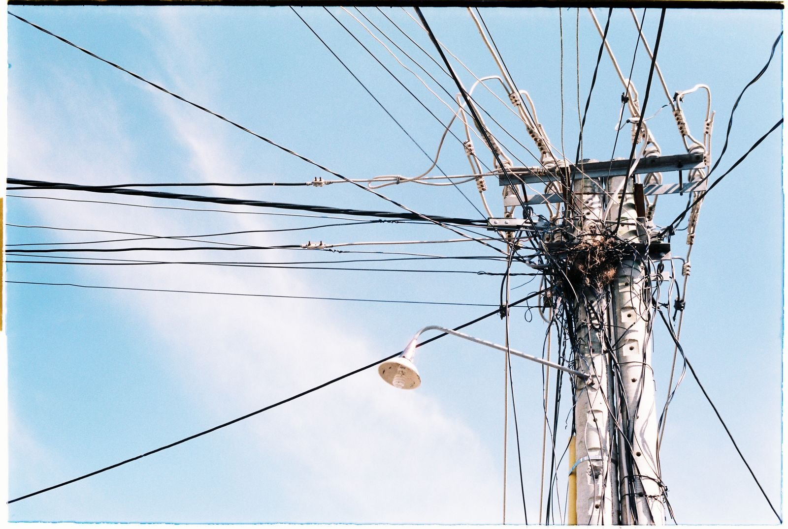 Poste com emaranhado de fios elétricos e uma luminária de rua contra o céu azul