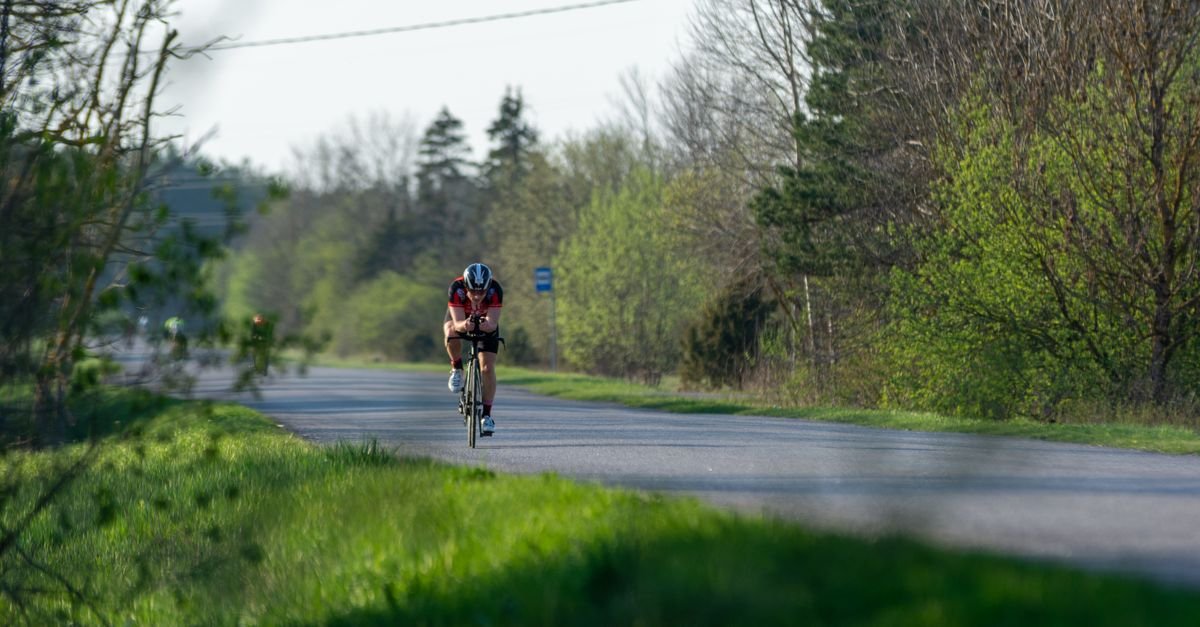 Ciclista pedala sozinho em estrada com mato verde nas margens