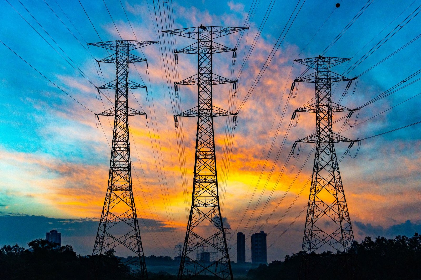 Três torres de transmissão de energia em silhueta contra um céu laranja e azul, imagem ilustrativa