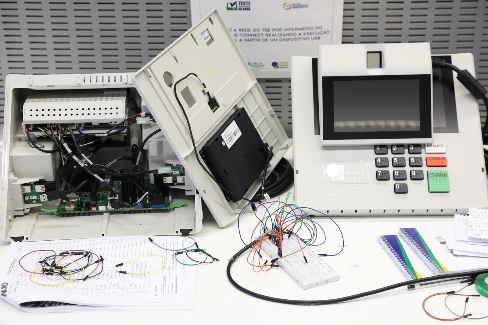 Urna eletrônica modelo UE2022 ao lado de outro equipamento com a carcaça aberta, em exibição do Tribunal Superior Eleitoral